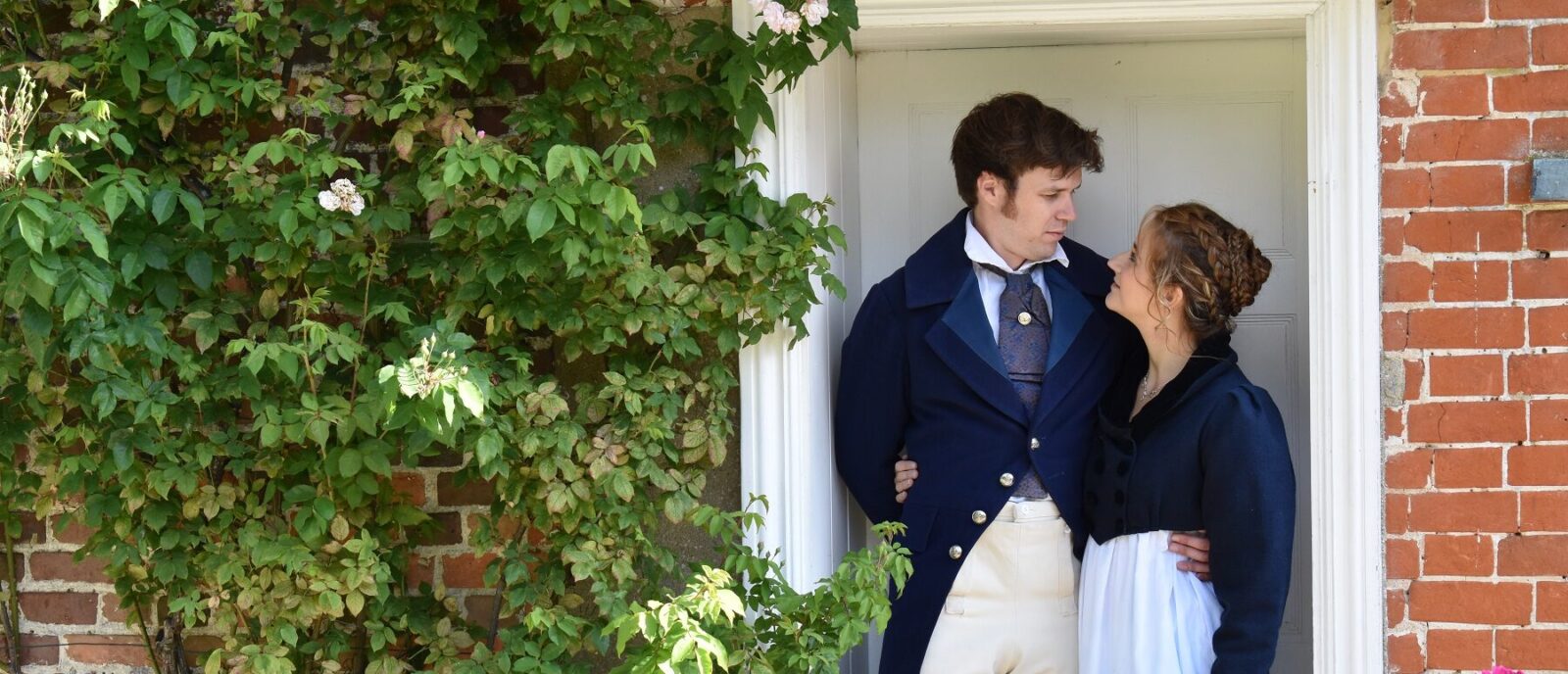 Actors portraying Captain Wentworth and Anne Ellliot from Persuasion standing in the doorway of Jane Austen's House