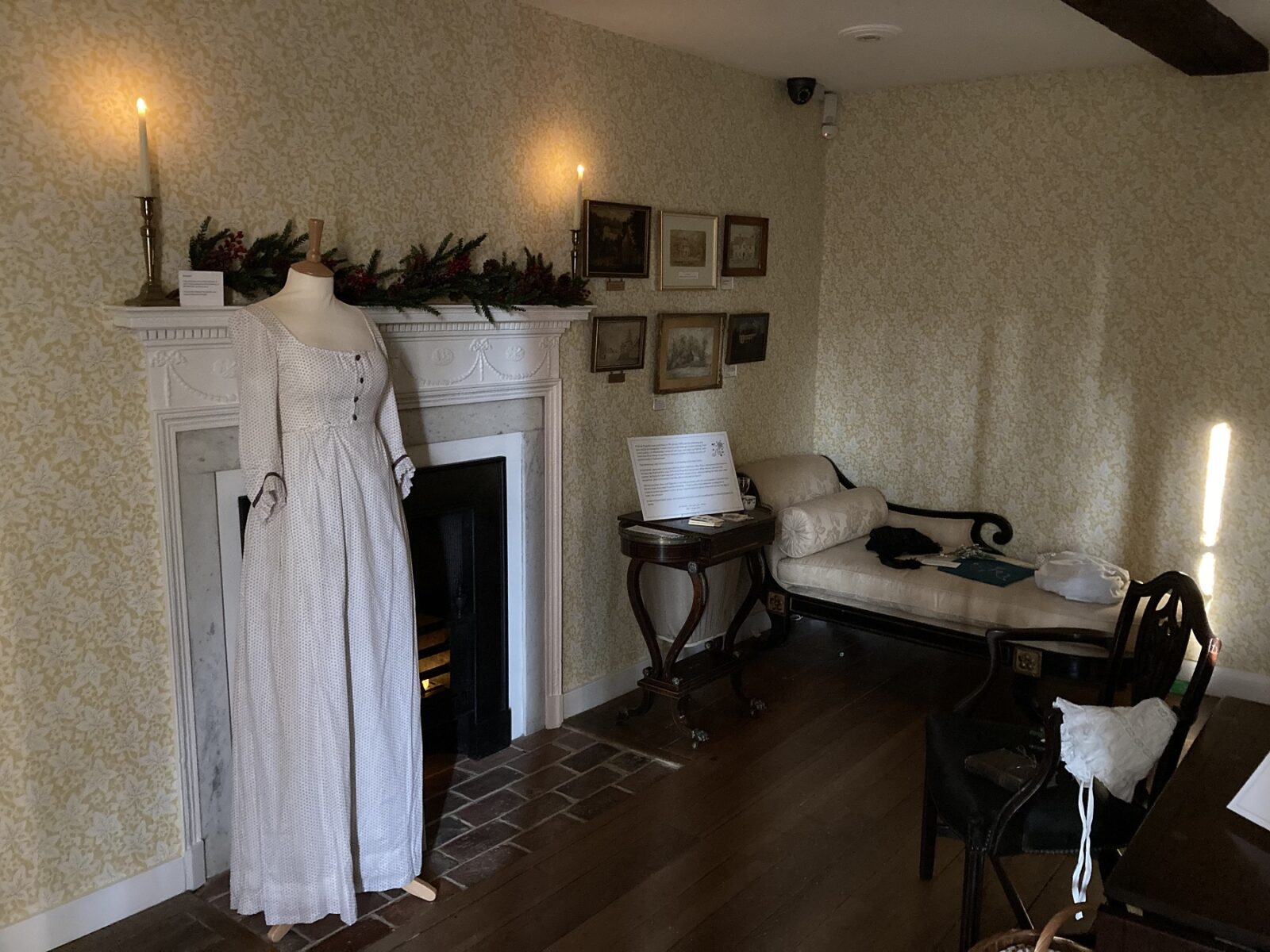 The Drawing Room at Jane Austen's House, with a Hepplewhite armchair owned by the Austens pulled up to the fire. A mannequin wears a day dress from 'Becoming Jane'