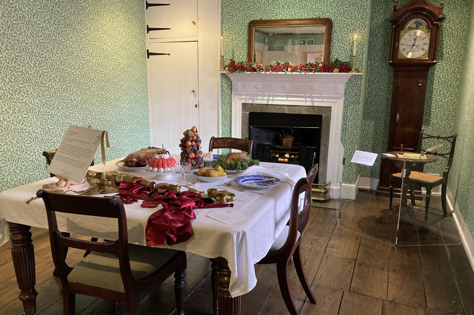 The Dining Room table is laid with 'cut up silk and gold paper' as well as a haunch of roast venison, roast partridge, a tower of fruits and a decorated jelly. Behind it, the fire crackles in the grate...