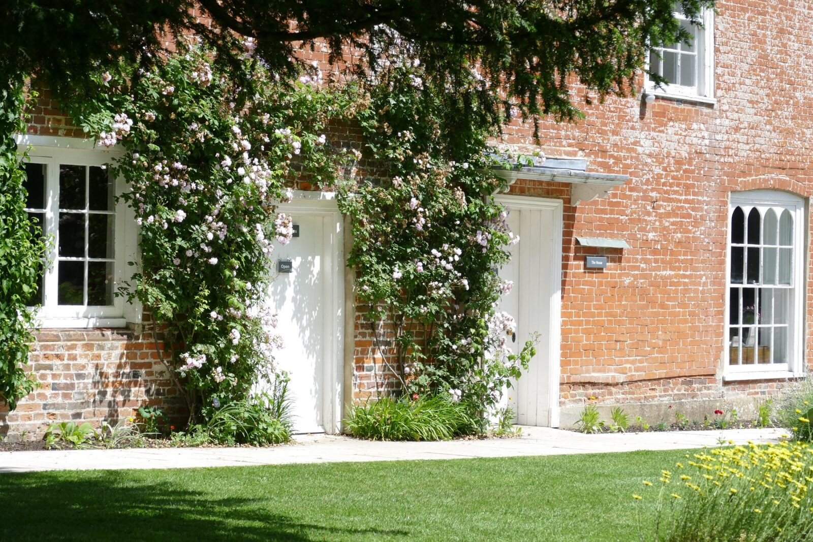 An image of the first floor of a red brick house, with two white doors. Roses surround the doors.