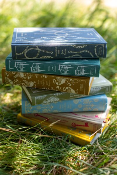 A stack of Jane Austen novels in the sunlight on the grass