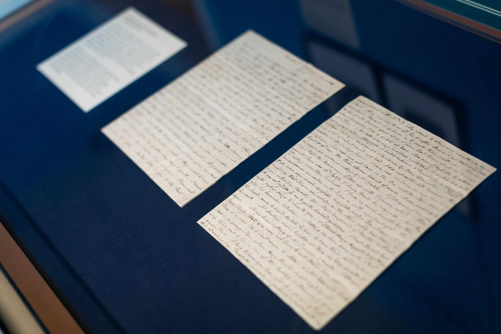 A close up of a two page letter written by Jane Austen, against a blue background in a display case
