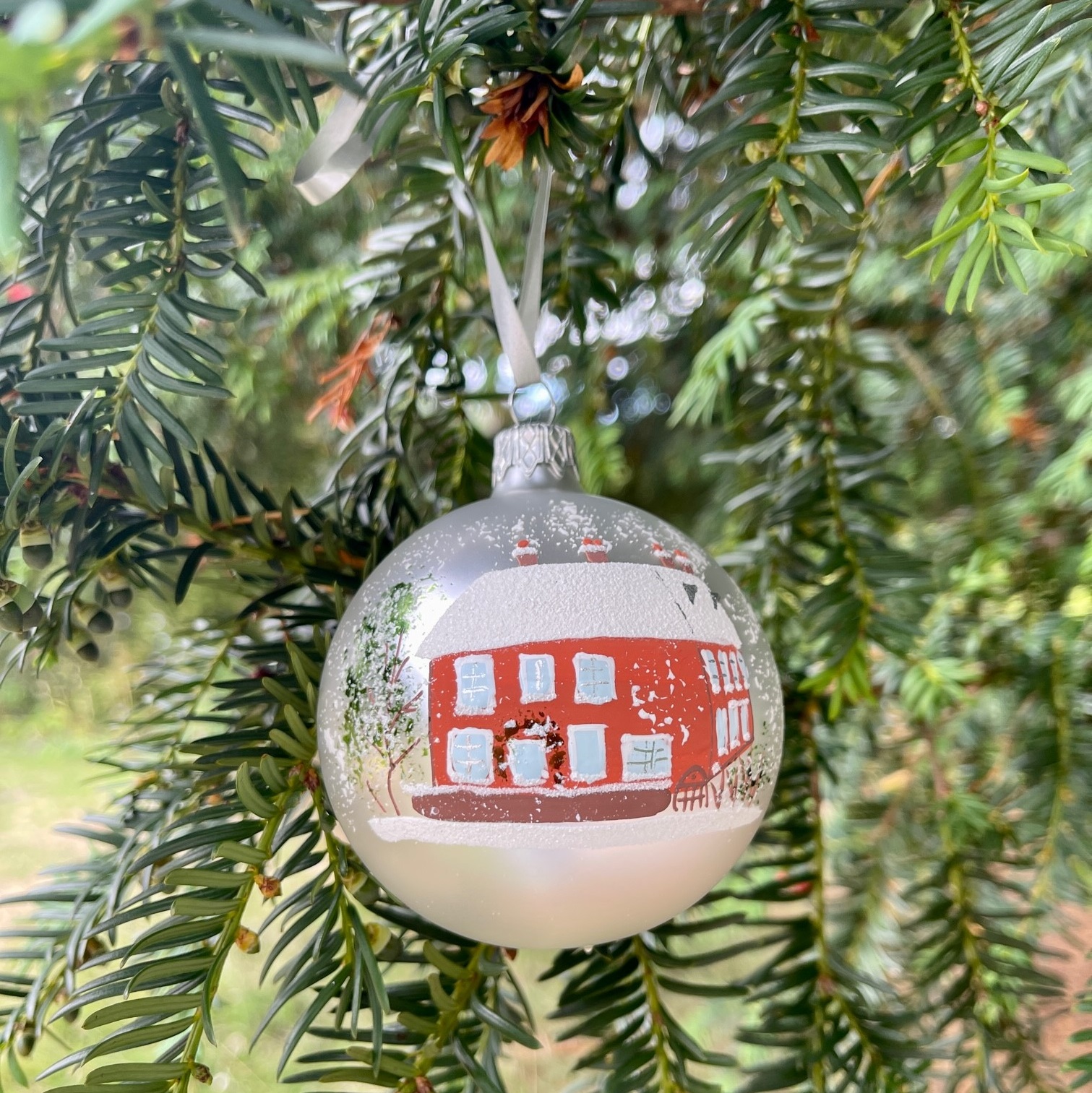 A silver Christmas bauble depicting Jane Austen's House in red, hanging on a Christmas tree