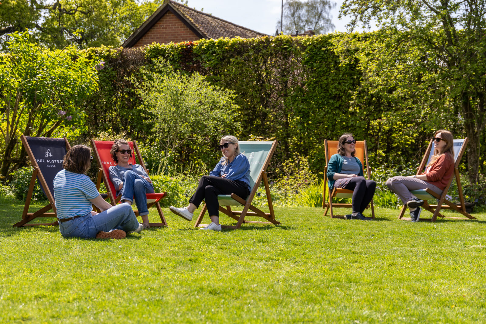Visitors relaxing in the sun on colourful deckchairs in the garden of Jane Austen's House