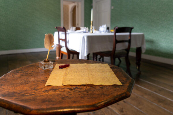 Jane Austen's small wooden writing table. A quill and letter sit on the table. 